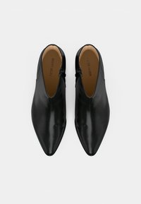 Černé kožené kotníkové boty s špičatou špičkou, s nízkým střihem a bočním zipem. Hladká textura, minimalistický styl.