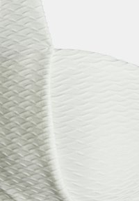 Tecido branco com um padrão texturizado e ondulado. O material é suave, apresentando um acabamento liso e um brilho subtil no desenho.