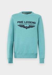 Tirkizni dukserica s okruglim izrezom, dugim rukavima i rebrastim manžetama. Ima natpis "PME LEGEND AMERICAN CLASSIC" i grafiku krila u tamnoplavoj boji.