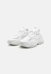 Weiße Sportschuhe mit einem gepolsterten Design, strukturiertem Mesh-Obermaterial, kontrastierenden grauen Akzenten und einer dicken, skulptierten Sohle. Mit Schnürverschluss.