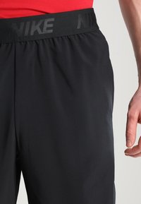Schwarze Sportshorts mit einer glatten Textur, ausgestattet mit einem breiten, elastischen Bund, auf dem "NIKE" eingeprägt ist. Nahaufnahme, die das Design und die Passform hervorhebt.