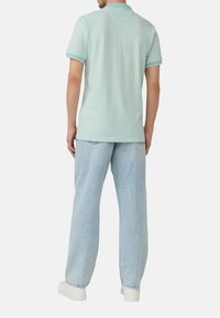 Mintgroene polo met korte mouwen en een kraag, gecombineerd met lichtblauwe, losse spijkerbroeken en witte sneakers.