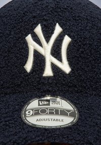 Casquette ajustable bleu marine en tissu texturé avec un logo "NY" brodé en blanc sur le devant ; étiquette indiquant "New Era 9FORTY."