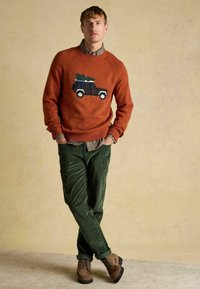 Oranžist kudumüts, millel on jõulupuu kujutisega veoauto, kombineeritud tumeroheline sametpükside ja pruunide nööpidega saapadega.