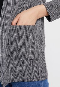 Šedá a bílá látka s kostkovaným vzorem hounds tooth, s boční kapsou, má měkkou strukturu a pevný design. Ins un casual fit style.