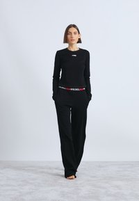 Μαύρο σετ με μακρυμάνικη μπλούζα και φαρδιά παντελόνια, από βαμβακερό υλικό, με μικρό λογότυπο στο στήθος και ελαστική ζώνη μέσης με το εμπορικό σήμα.