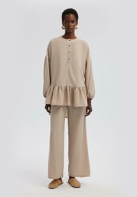 Top beige relajado con escote redondo, placket de botones y dobladillo con volantes, combinado con pantalones de pierna ancha a juego. Material texturizado.