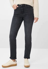 Jeans in denim nero con vestibilità slim, dotati di una vita classica, chiusura con bottone metallico e design a cinque tasche. Abbinati a sneaker color crema.