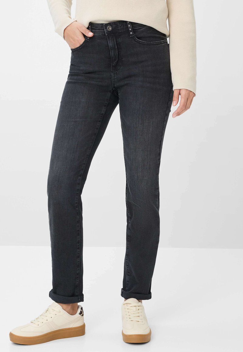 Jeans in denim nero con vestibilità slim, dotati di una vita classica, chiusura con bottone metallico e design a cinque tasche. Abbinati a sneaker color crema.