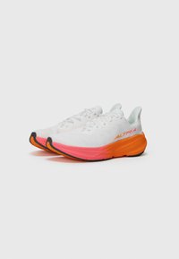White athletic shoes featuring a textured upper, pink and orange sole, and a sleek design with laces and branding on the side.