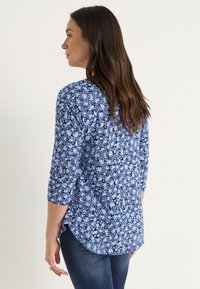 Blauwe bloemenblouse met driekwartmouwen, met een mix van lichte en donkere blauwe patronen, ronde zoom en zachte stofstructuur.