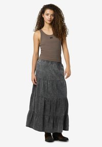 Rudas kamšelis ir pilka, sluoksniuota maksi sijonas su elastingu juosmeniu ir minkšta tekstūra. Aukšti, plokšti juodi batai matomi apatiniame krašte.