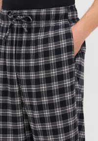 Črne in bele karirane pižamne hlače z elastičnim pasom, z vrvico in stranskimi žepi; mehak material s karirastim vzorcem.