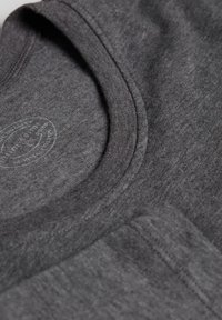 Szara bawełniana koszulka z okrągłym dekoltem, charakteryzująca się gładką strukturą i małym nadrukowanym logo przy dekolcie.