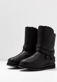 Schwarze Knöchelstiefel aus glattem Wildleder mit einem weichen Kunstfellfutter, ausgestattet mit einem gewickelten Riemendesign und strukturierten Sohlen für besseren Halt.