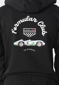 Černá mikina s grafickými potisky zeleného závodního auta, textem "Formula Club" a "Pas de Monaco" s designem šachovnicového štítu.