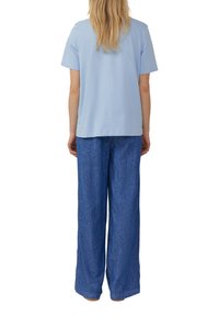 T-shirt bleu clair à manches courtes associé à un pantalon large, sombre et ample, le tout en tissu doux et texturé.