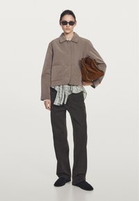Brown cropped corduroy jacket with large buttons, layered over a plaid shirt. Dark brown wide-leg pants and black slip-on shoes. Holding brown bag.