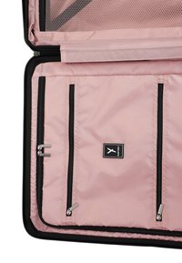 Světle růžový textilní organizér se třemi zipovými kapsami, černými akcenty a síťovanou částí. Štítek zobrazuje logo značky na černé etiketě.