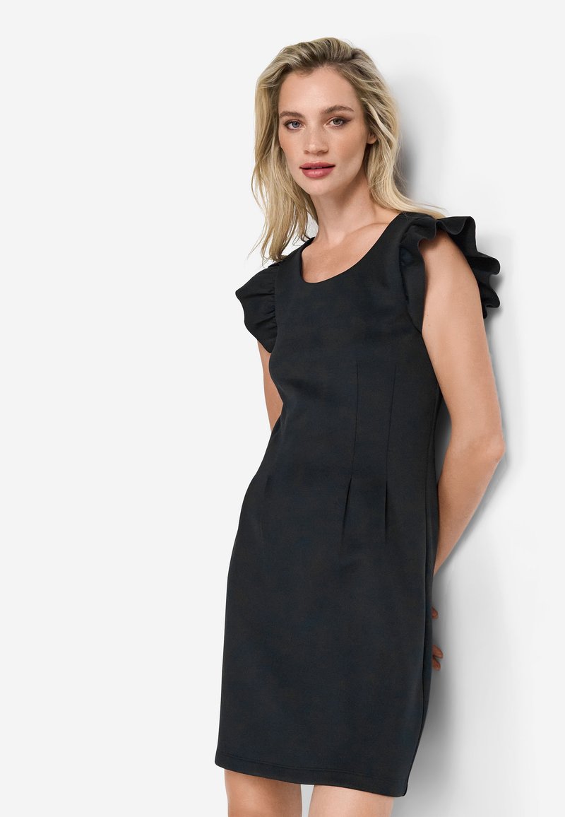 Vestido negro con mangas cortas acampanadas, cuerpo ajustado y pliegues en la cintura; textura suave y longitud por encima de la rodilla.