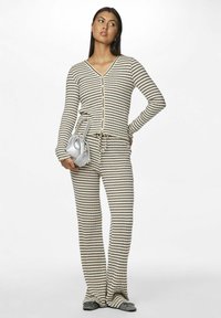 Ensemble de loungewear rayé en beige et noir, comprenant un cardigan ajusté avec des boutons et un pantalon à jambes larges. Le matériau semble doux et côtelé.