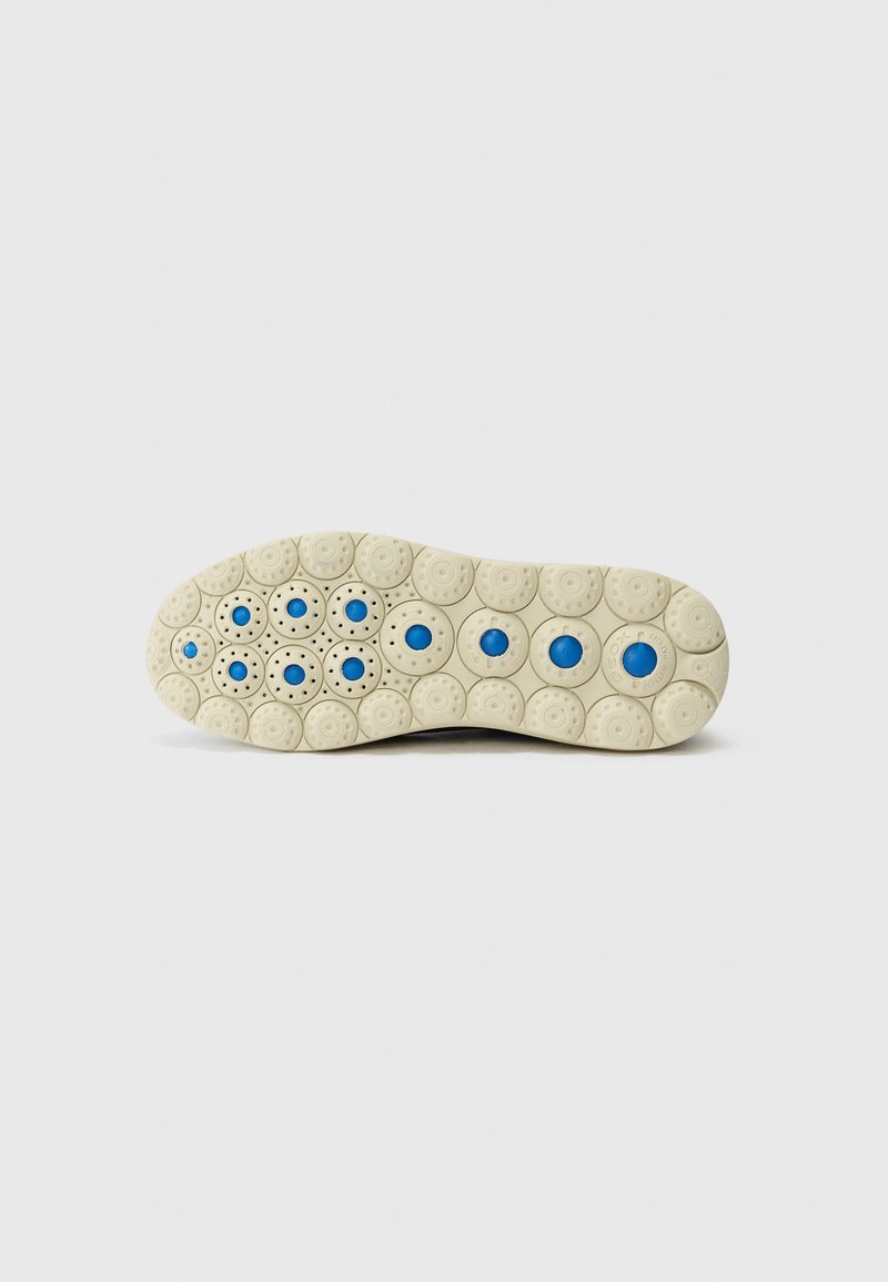 Suela de zapato con un patrón redondeado en beige claro, que presenta acentos circulares azules. La superficie está texturizada con pequeñas perforaciones para mayor agarre.