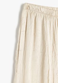 Lichtbeige rok met een gekreukt textuur, elastische tailleband en zijsplitten voor beweging. Gemaakt van een lichte stof.