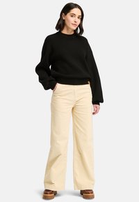 Svart ribbad stickad tröja med långa ärmar, som är ihopkopplad med vida beigea kordbyxor. Inkluderar en liten logotag nära midjan.