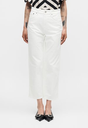 Inimene kannab kõrge vöökohaga valgeid lühikesi laiade säärtega pükse esitaskutega ning musti teravate ninaga madalaid kingi metallist pannaldega.