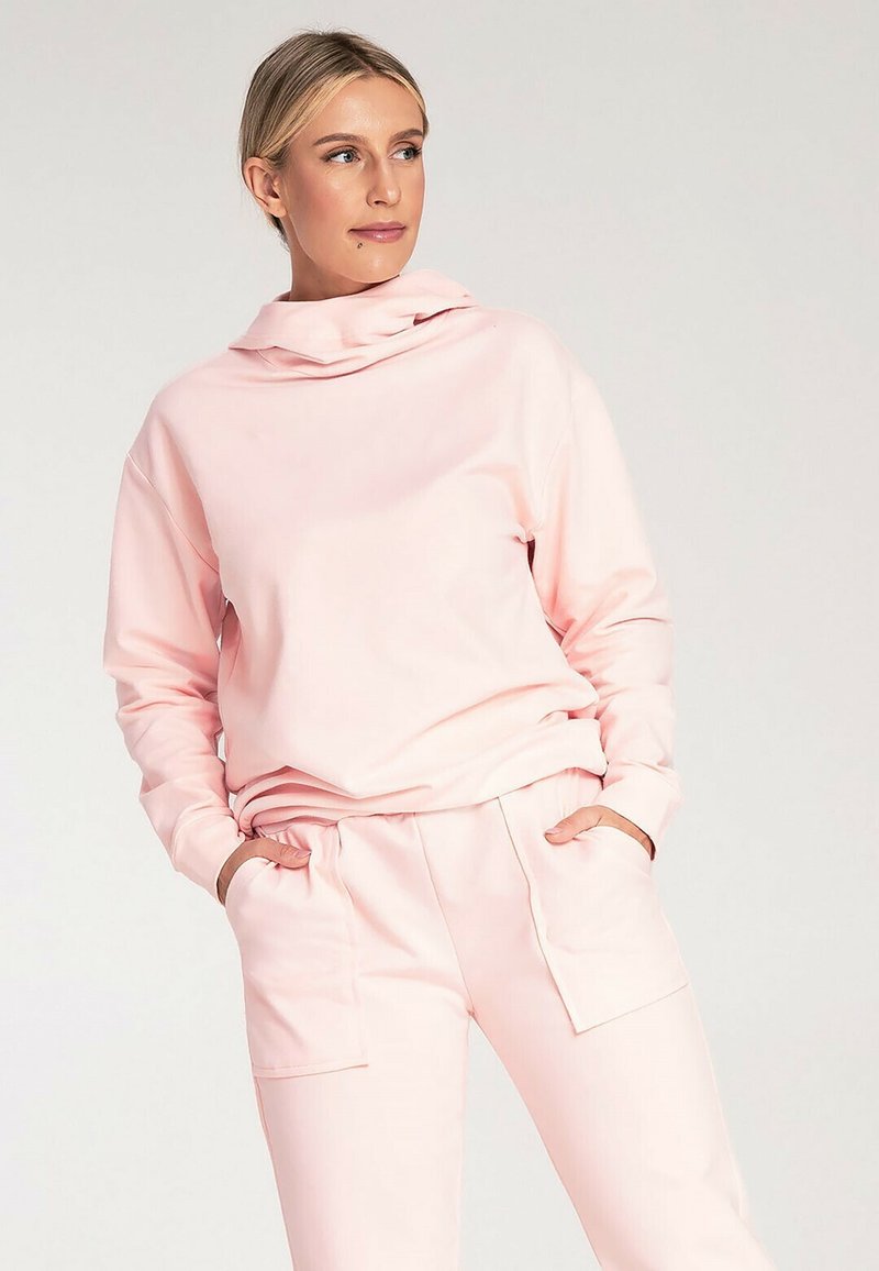 Różowa bluza z kapturem wykonana z miękkiego materiału, charakteryzująca się luźnym krojem, długimi rękawami i kieszenią typu kangur, zestawiona z pasującymi spodniami.
