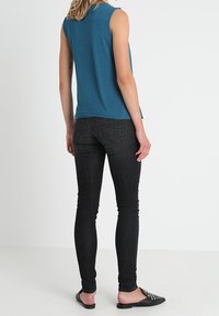 Turkos ärmlös topp, svarta tajta jeans och svarta slip-on skor. Slät tyg, åtsittande form, minimal detaljering och inga synliga mönster.