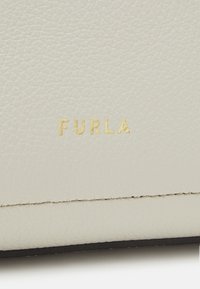 Vit texturerad läder med en guldprägling av "FURLA"-logotypen. Sömmen är synlig längs kanten, vilket ger en ren och sofistikerad finish.