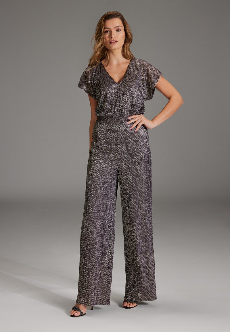 Fioletowy kombinezon w wzory z dekoltem w serek, krótkimi rękawami, wcięciem w talii oraz szerokimi nogawkami, o błyszczącej fakturze materiału.