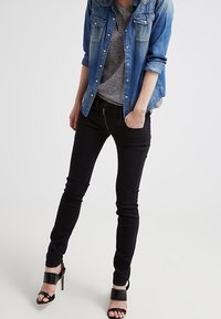 Denim shirt in light blue with button details, gray T-shirt, black skinny jeans, and black heeled sandals.