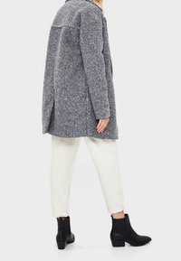 Gray textured coat, mid-length, relaxed fit. Paired with white rolled-up pants and black ankle boots. Simple, functional design.