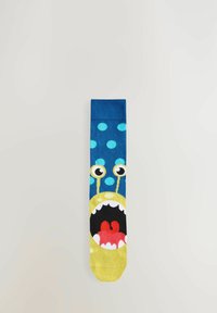 Chaussettes bleues avec un design de monstre jaune, ornées de pois, de grands yeux et d'une bouche ouverte laissant apparaître des langues rouges. Texture en tricot douce.
