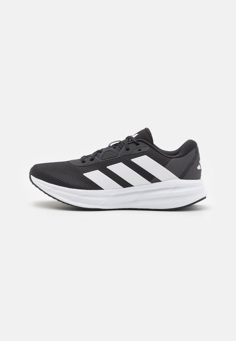 Chaussure de sport noire avec un dessus en maille texturée, design à trois bandes blanches, semelle rembourrée et semelle en caoutchouc noire.