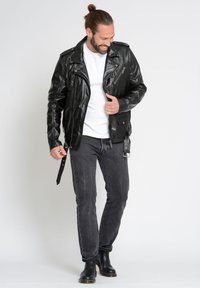 Czarna skórzana kurtka motocyklowa z zamykanymi kieszeniami, dopasowany krój i srebrne akcesoria, w zestawie z szarymi dżinsami i czarnymi butami.