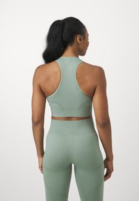 Camiseta deportiva de color verde claro con diseño de espalda racer, combinada con leggins de tiro alto a juego, que presentan un material texturizado acanalado.