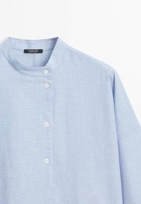 Chemise en lin bleu clair avec col mandarin et boutons blancs sur le devant, étiquette Massimo Dutti.