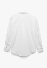 Camisa blanca de manga larga hecha de tejido suave, con cuello tipo polo, detalle de pliegue en la parte posterior y dobladillo redondeado. Puños abotonados con un solo botón.
