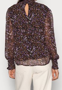 Transparente, schwarze Bluse mit floralem Muster, die lila und braune Akzente aufweist, mit hohem Kragen und einem Schlüsselloch-Rücken sowie gerafften Manschetten an den langen Ärmeln.
