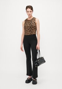 Brun leopardmønster crop-top, svarte tettsittende bukser, svart lakkveske med gulldetaljer, og kraftige svarte platåski.