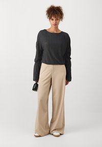 Haut noir à manches longues et côtelé associé à un pantalon beige à jambes larges. La tenue présente un design cropped et un sac à main noir élégant.