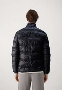 Sort pufferjakke med en skinnende finish, ribbet tekstur, høj krave og horisontale syninger. Har en afslappet pasform.