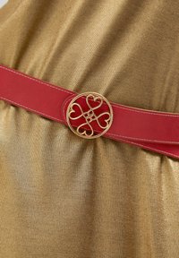 Röd läderbälte med ett guld cirkulärt spänne med hjärtmotiv, kombinerat med en klänning i guld av texturerad tyg.