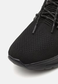 Zapatilla de correr negra con una parte superior de punto texturizado, con puntera de goma y cordones planos. Presenta un collar acolchado y una suela duradera para tracción.