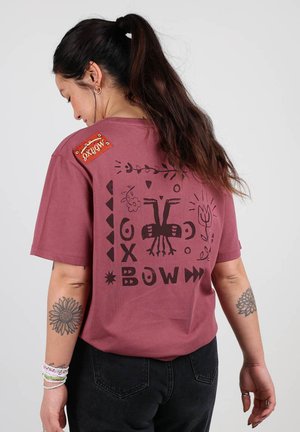 T-shirt en coton bordeaux avec un design graphique noir comprenant des formes et des motifs abstraits à l'arrière ; comprend une étiquette rouge sur l'épaule.