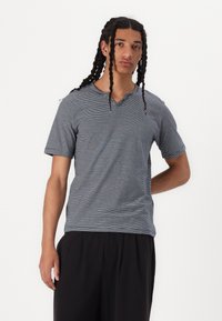 Välj lätt, gråstrimmig T-shirt med korta ärmar och V-ringning. Tyget har en slät textur. Modellen har matchat den med lösa svarta byxor.