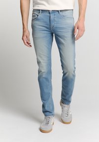 Lichtblauwe denim jeans met een slim fit, vervaagde textuur, vijf-pocket ontwerp en subtiele stikdetails, gecombineerd met grijze sneakers.
